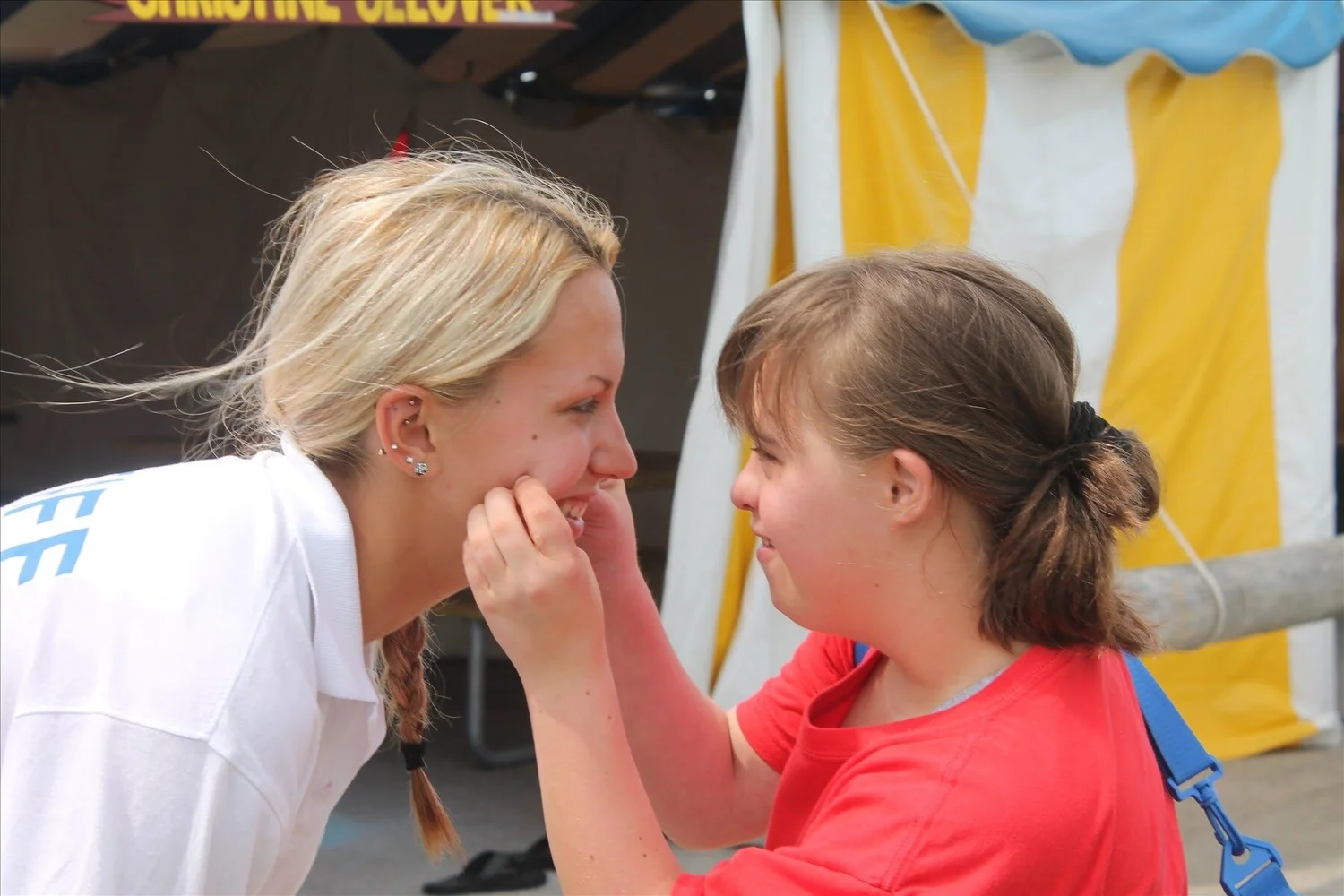 A volunteer and camper sharing a laugh face to face at a summer event