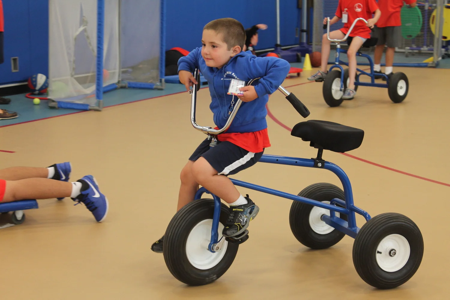 A young camper riding an adaptive tricycle in the gym