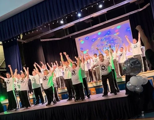 The full cast celebrating on stage with arms raised