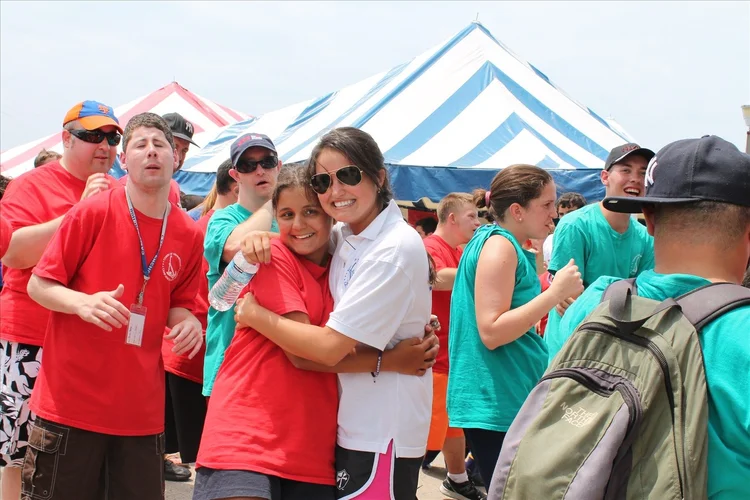 A Camp ANCHOR volunteer and camper sharing a hug in front of the event tents