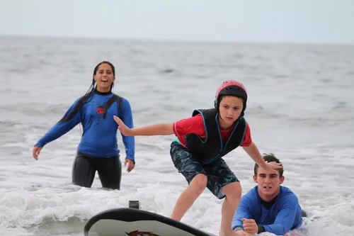 Camp ANCHOR campers surfing the ocean with a volunteer